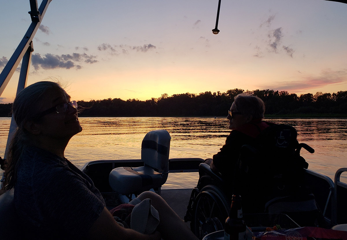 Christina Crosby and Janet Jakobsen seated on the boat, looking back towards camera with sunset in background.