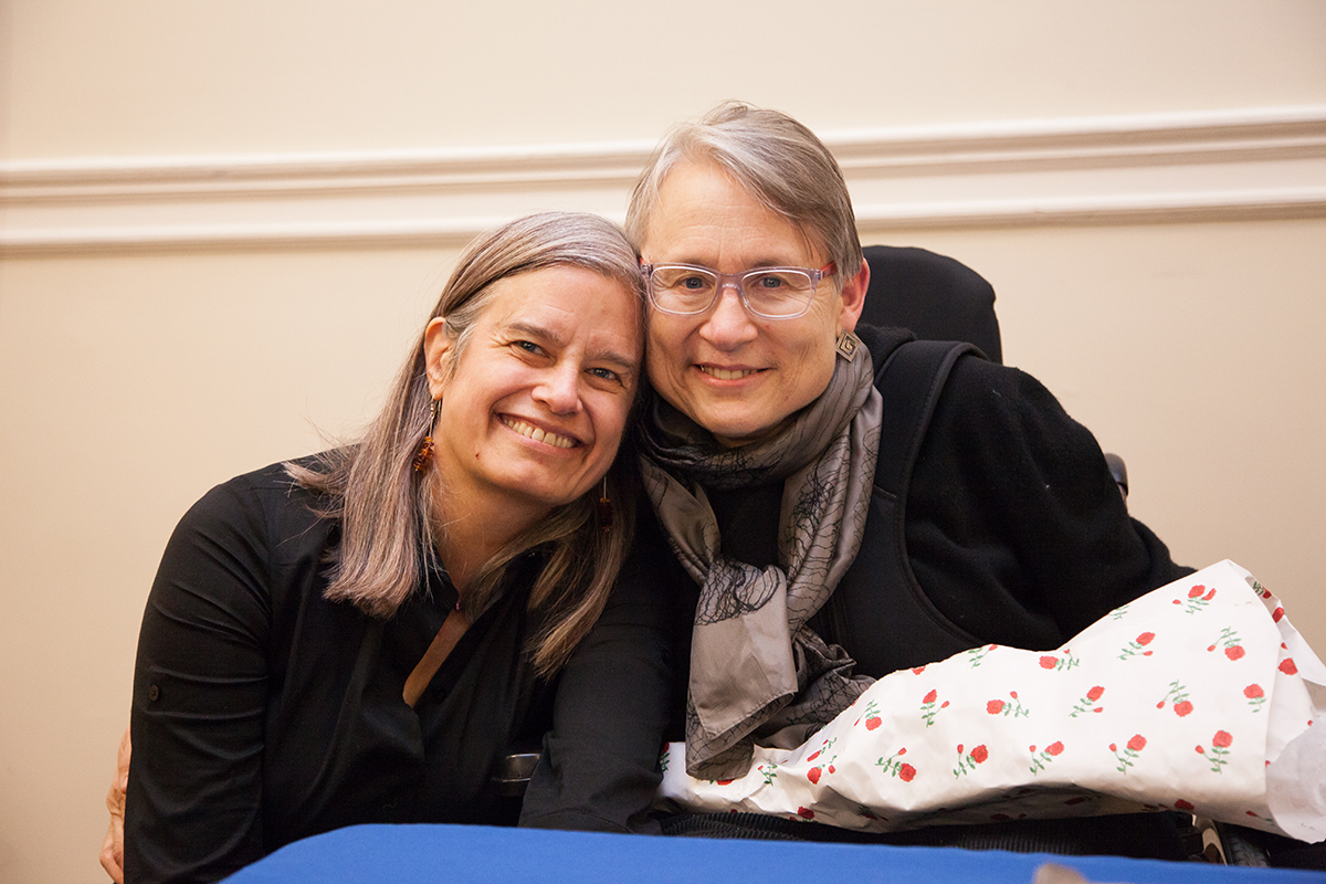 Photograph of Christina Crosby with a bouquet of flowers on her lap, with Janet Jakobsen